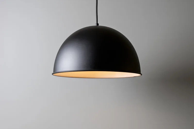 Matte black dome pendant lamp hanging from ceiling with warm glow against plain wall