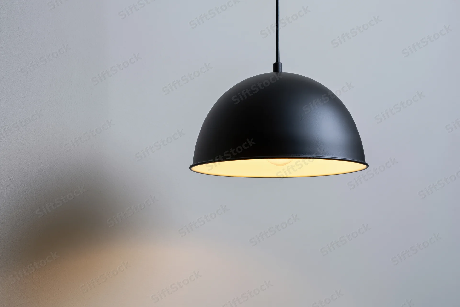 Matte black dome pendant lamp hanging from ceiling casting warm glow on wall