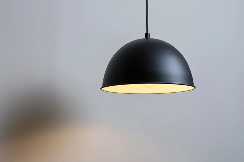 Matte black dome pendant lamp hanging from ceiling casting warm glow on wall