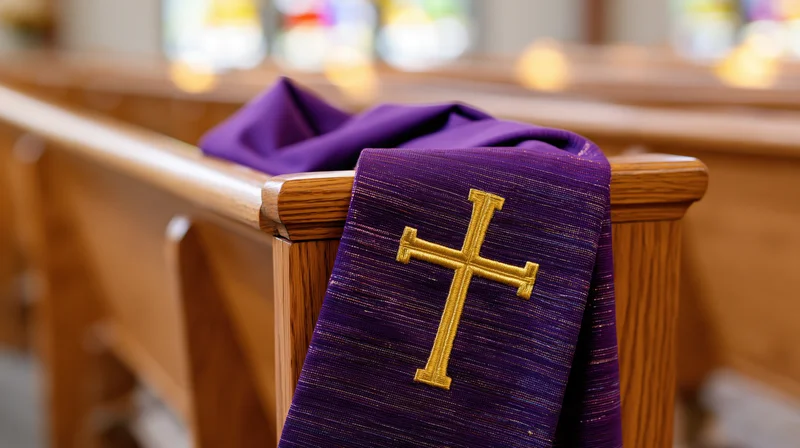 Purple liturgical stole with gold embroidered cross draped over wooden church pew