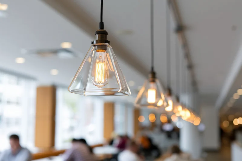 Row of edison bulb pendant lights with geometric clear glass shades hanging from ceiling in restaurant interior