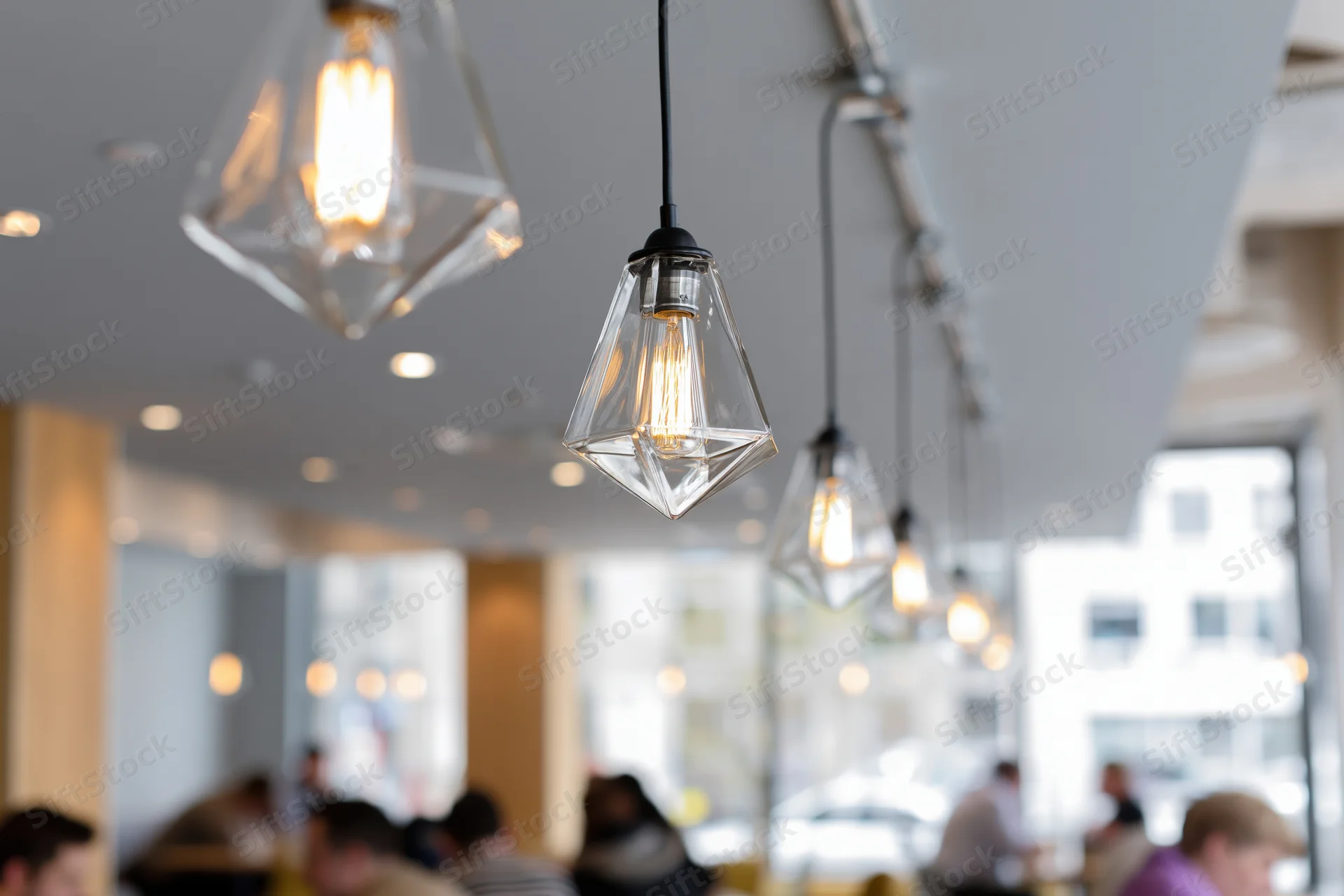 Row of geometric glass pendant lights with edison bulbs hanging from ceiling in cafe interior