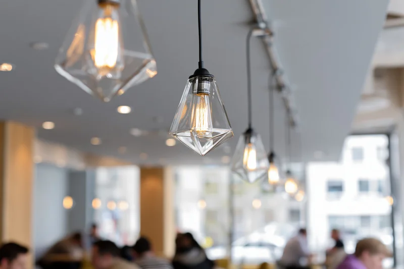 Row of geometric glass pendant lights with edison bulbs hanging from ceiling in cafe interior
