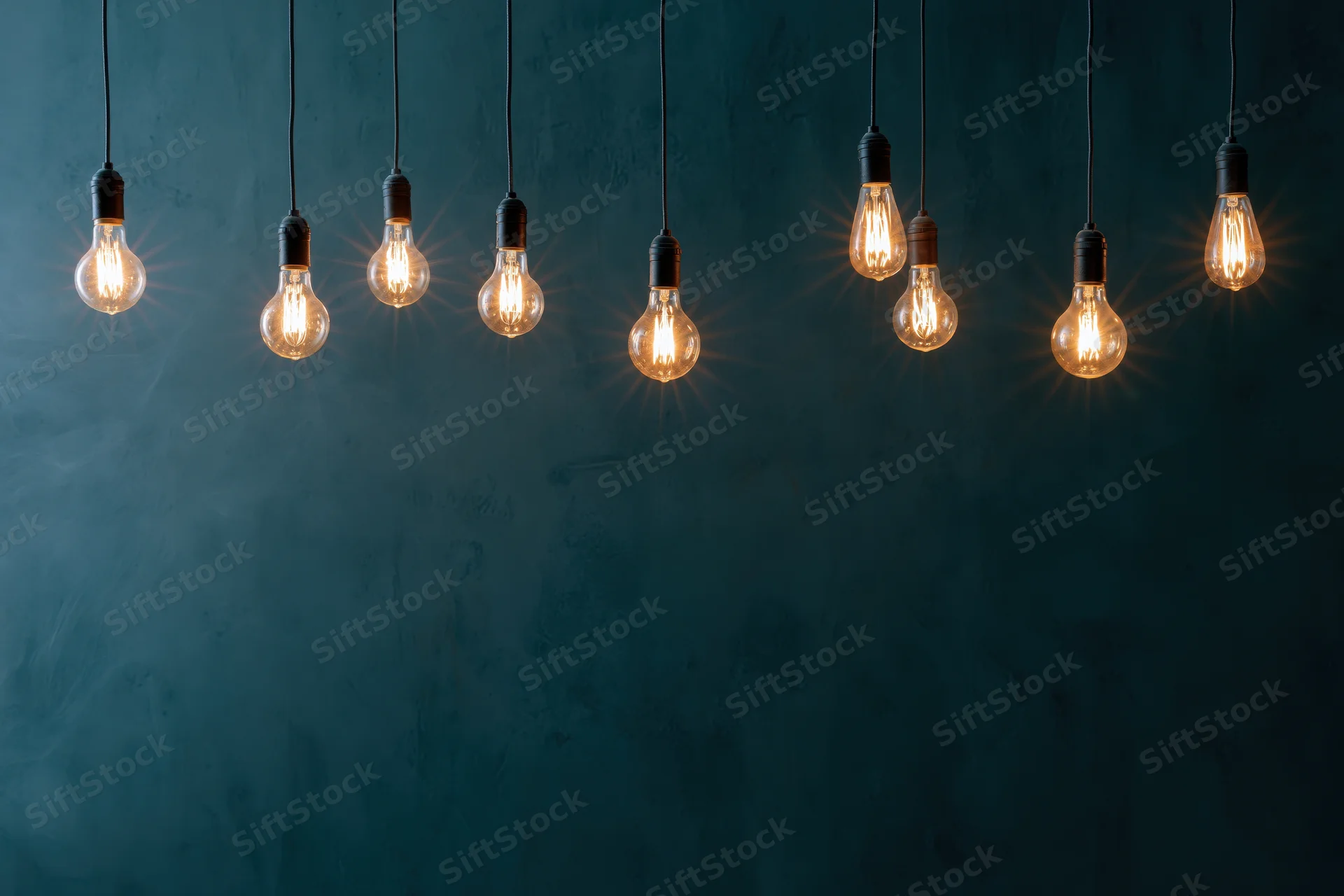 Row of glowing edison-style lightbulbs hanging from cords against a dark textured wall