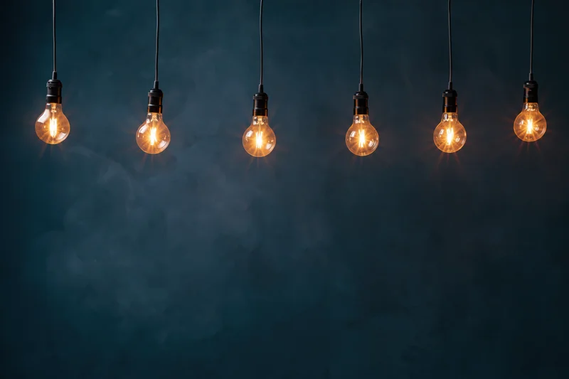 Row of glowing edison-style incandescent bulbs hanging from ceiling against dark blue background with copyspace below
