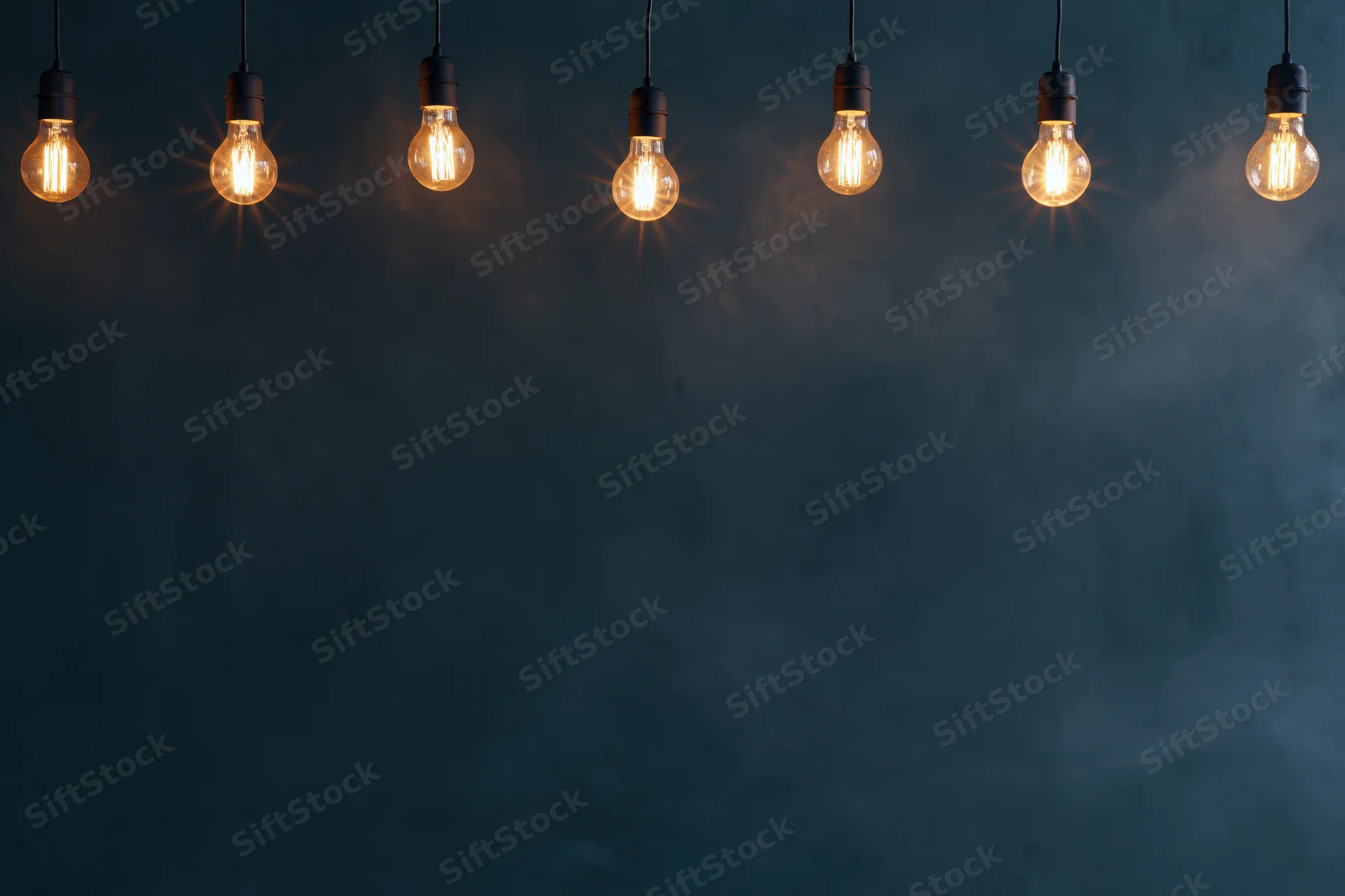 Row of glowing edison-style lightbulbs hanging against a dark textured wall with copyspace below