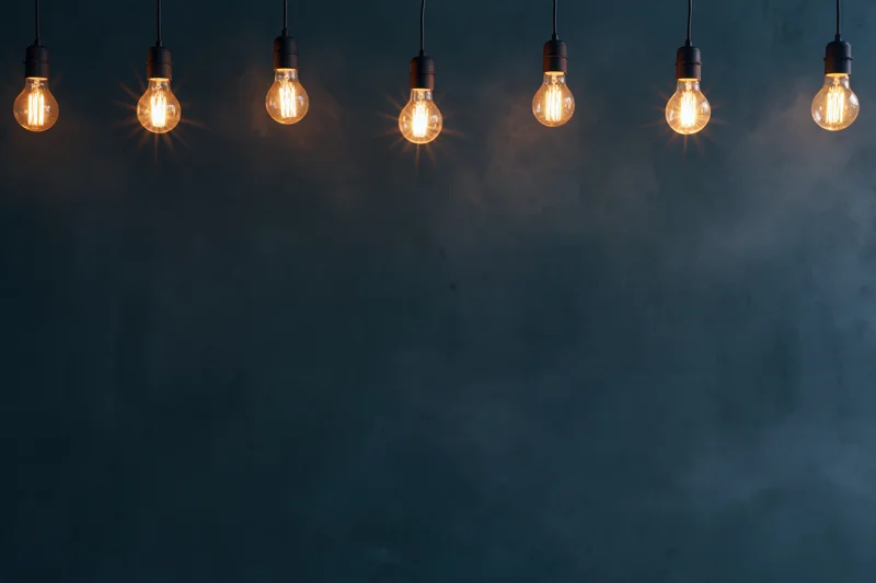 Row of glowing edison-style lightbulbs hanging against a dark textured wall with copyspace below
