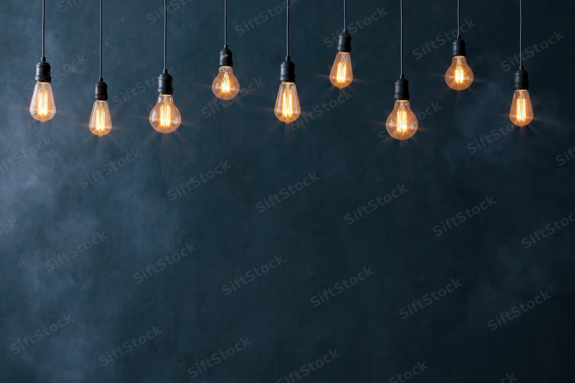 Row of glowing edison-style lightbulbs hanging against dark textured wall with copyspace below