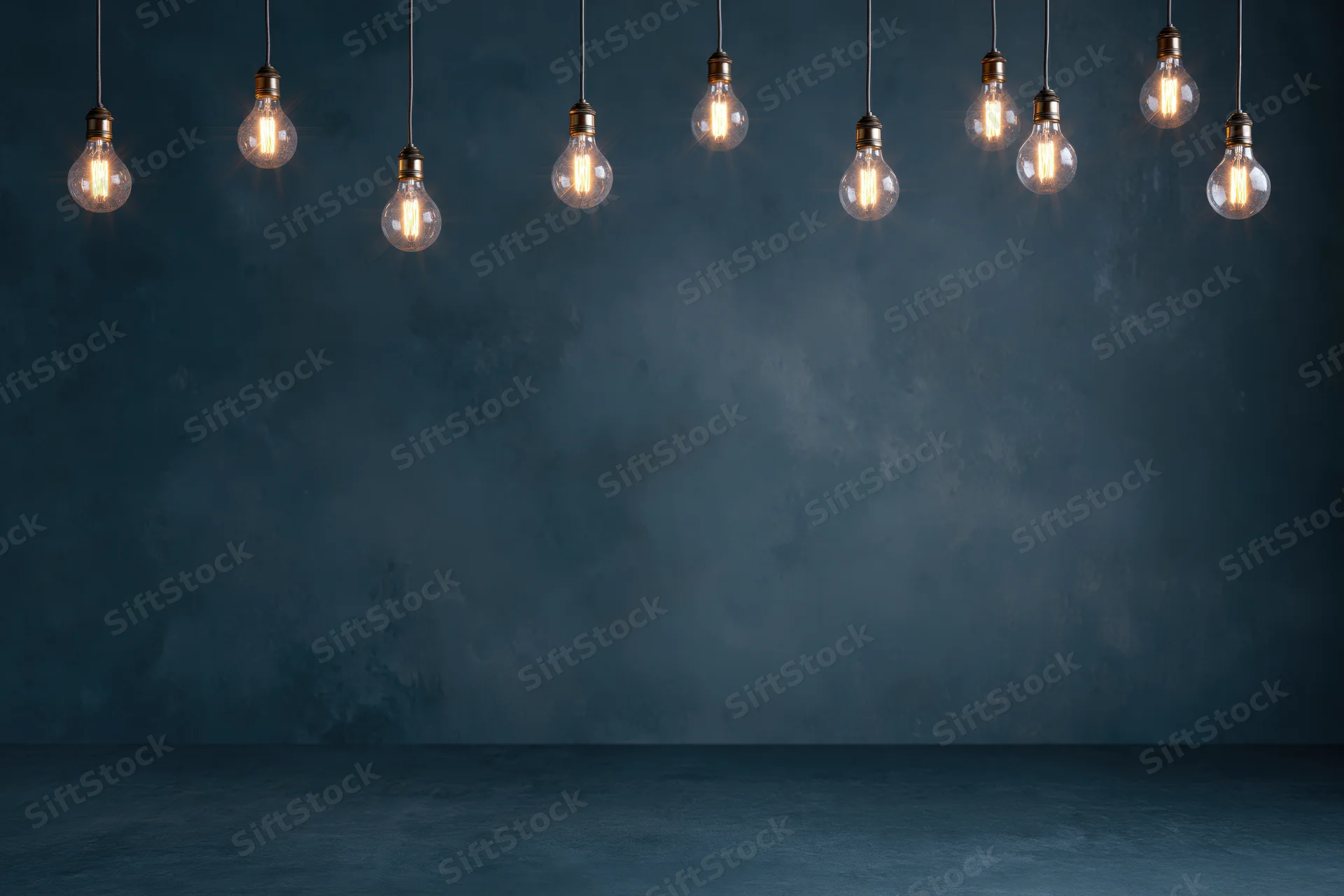 Row of illuminated incandescent bulbs hanging from cords against a dark blue concrete wall with copyspace below