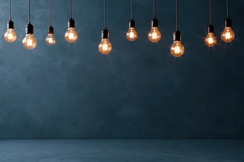 Row of glowing incandescent bulbs hanging from cords against a dark blue concrete wall with copyspace below