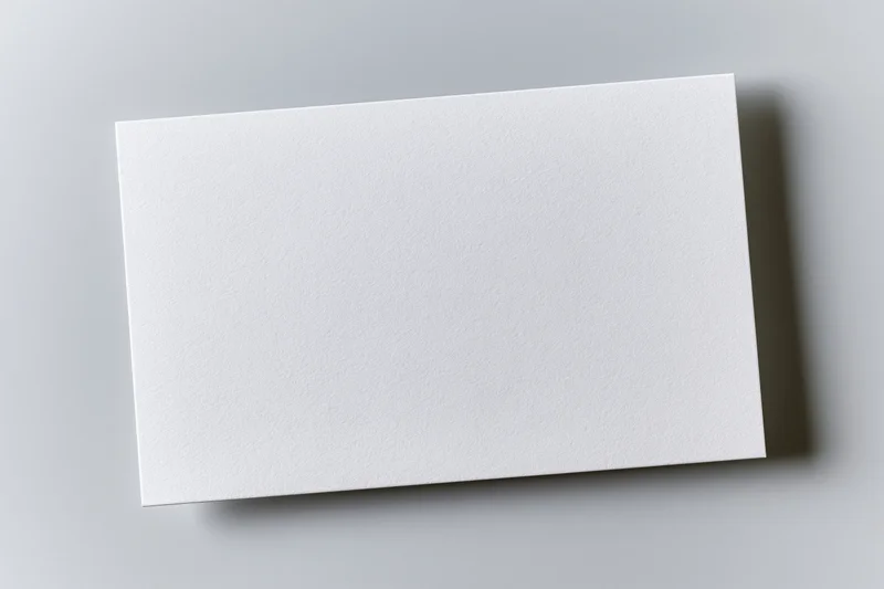 Blank white rectangular card lying flat on a gray surface with soft shadow and copyspace