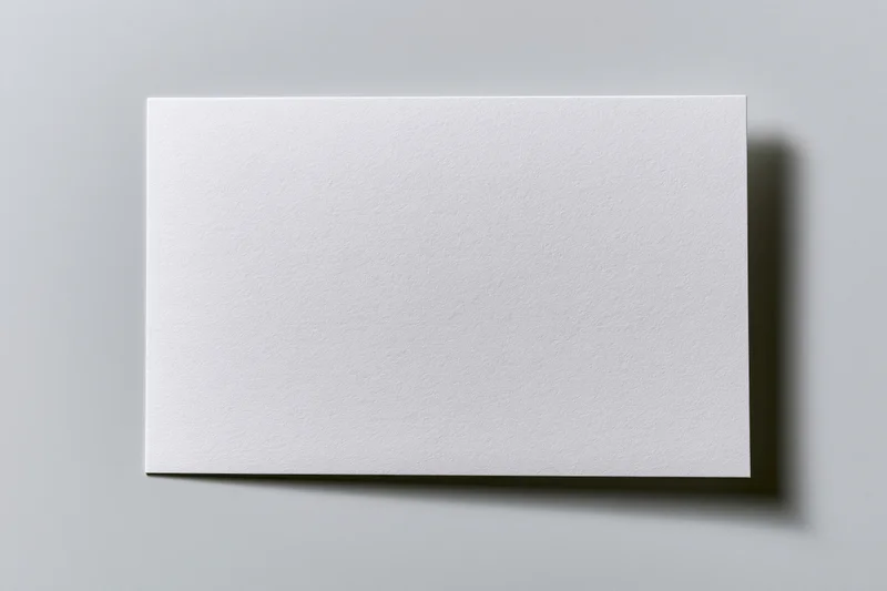 Blank white rectangular card lying flat on a gray surface with soft shadow