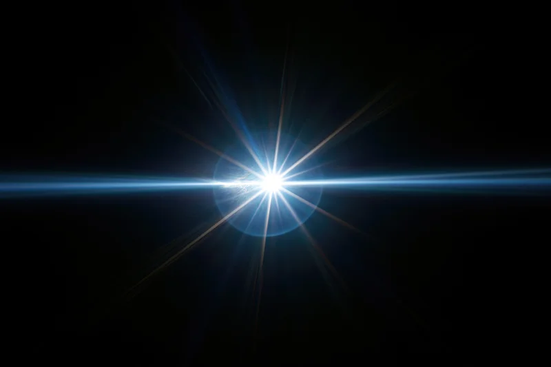 Bright blue-white lens flare centered on black background with radial light beams