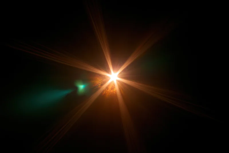 Bright point light source emitting starburst rays against dark background with teal glow on one side