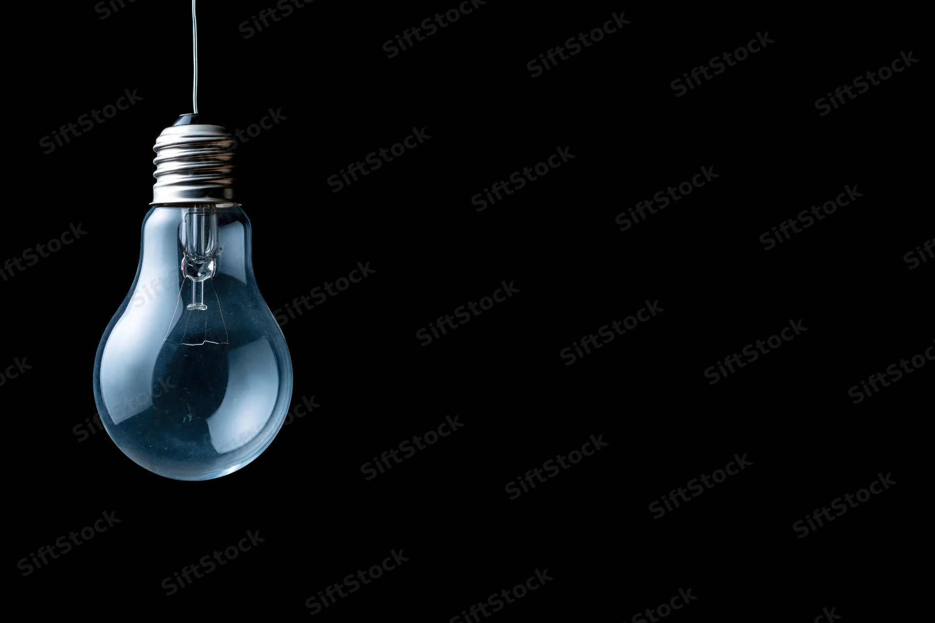 Unlit incandescent glass light bulb hanging from a wire against a black background