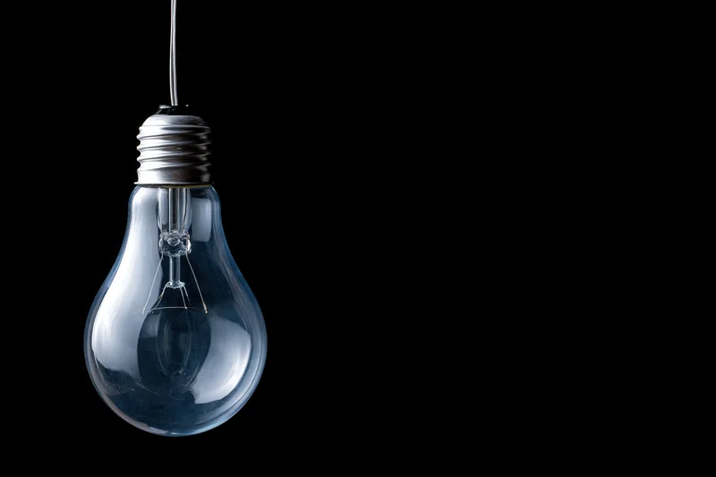 Unlit incandescent glass light bulb hanging from a wire against black background