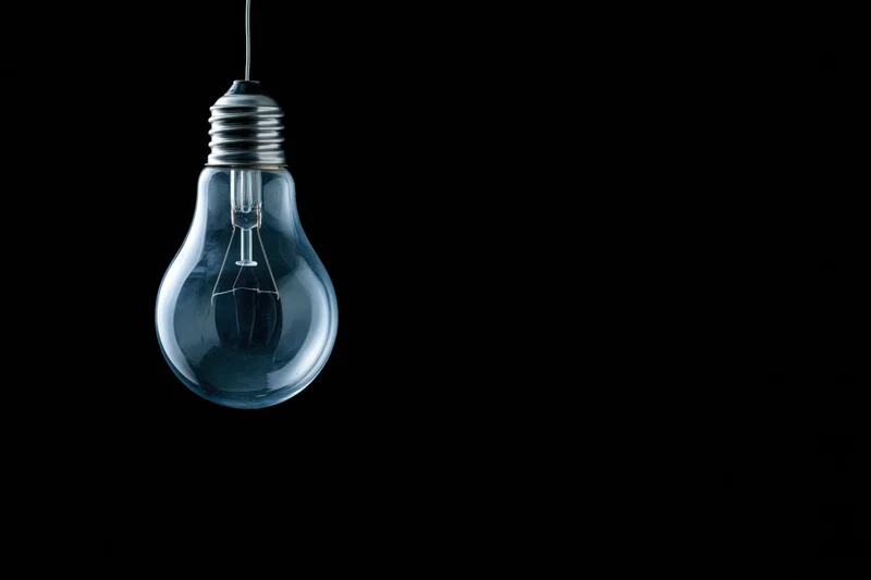 Unlit incandescent glass light bulb hanging from a wire against a black background
