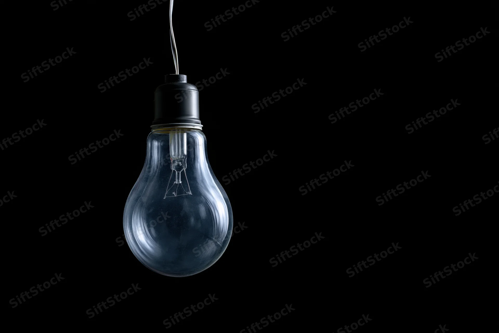 Unlit incandescent glass light bulb hanging from a wire against a black background