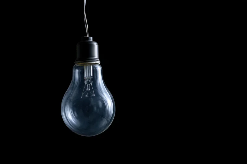 Unlit incandescent glass light bulb hanging from a wire against a black background