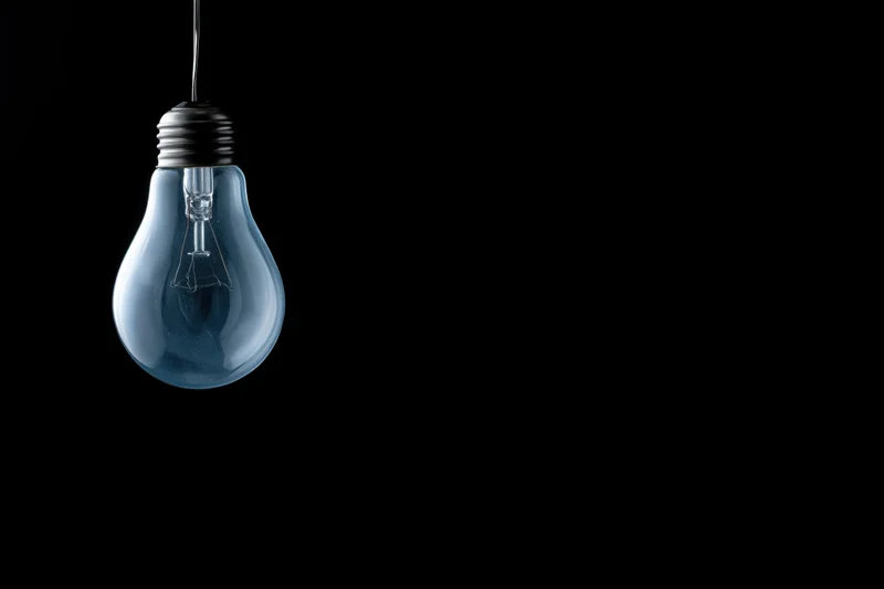 Unlit incandescent glass light bulb hanging from a wire against a black background