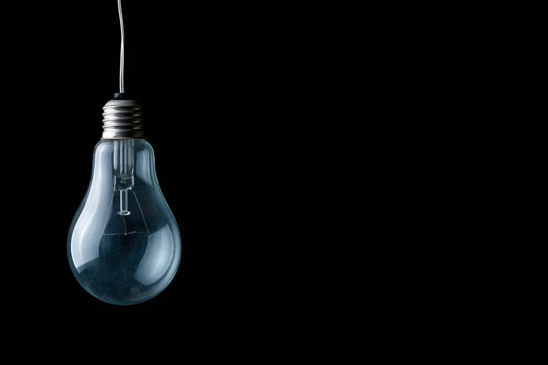 Unlit incandescent glass light bulb hanging from a wire against a black background