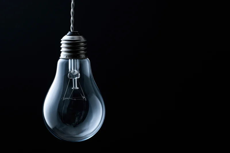 Unlit incandescent glass light bulb hanging from a wire against a black background