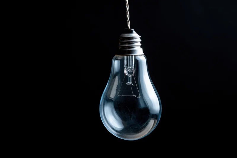 Unlit incandescent glass light bulb hanging from a twisted wire against a black background