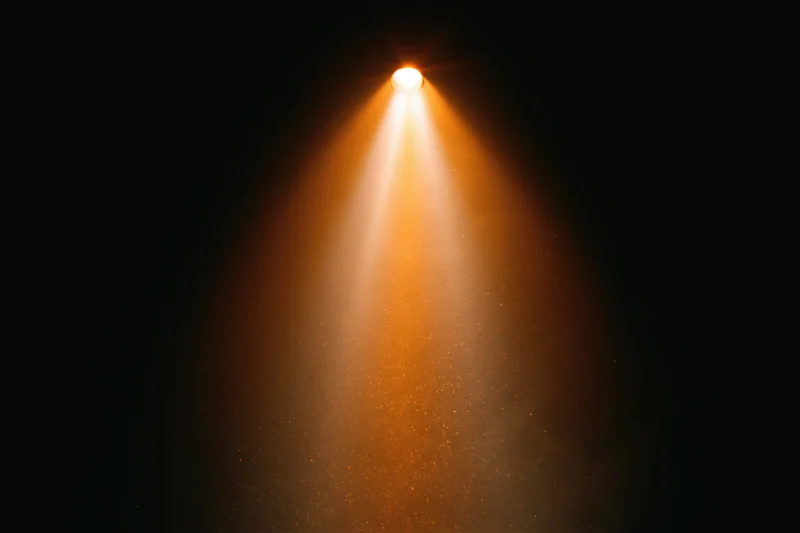 Warm amber spotlight beam shining downward in dark theater space