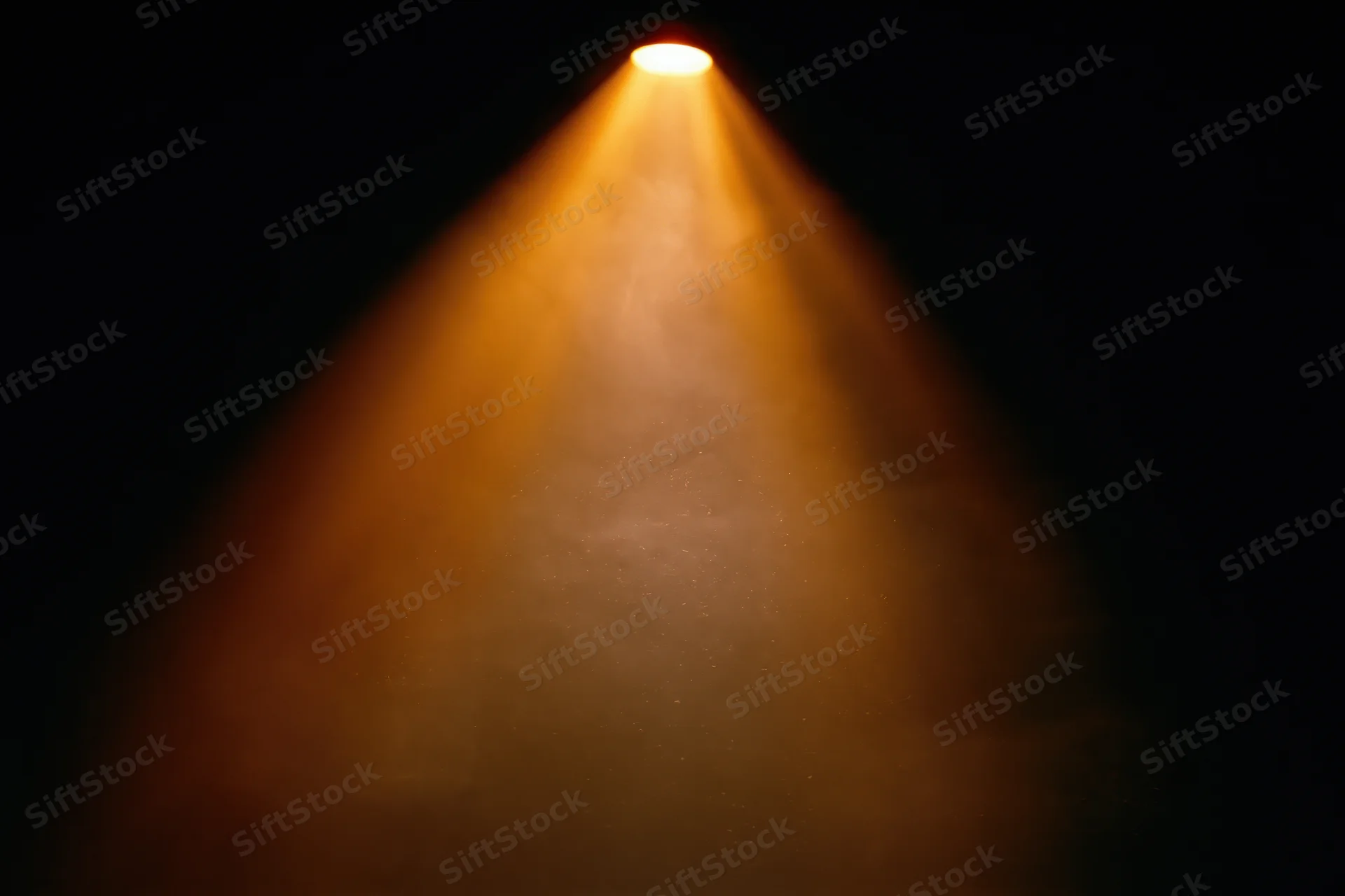 Warm amber spotlight beam shining downward from ceiling in dark theater setting