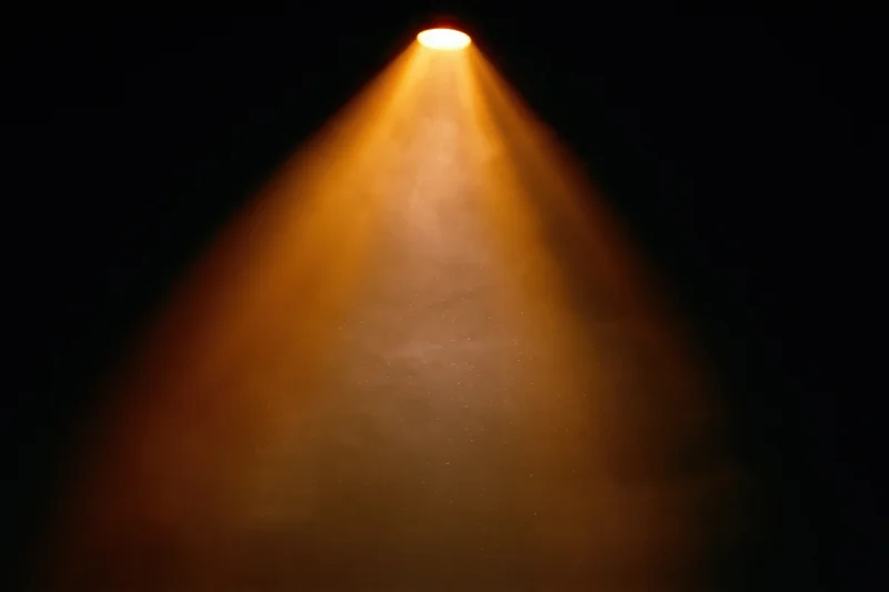 Warm amber spotlight beam shining downward from ceiling in dark theater setting