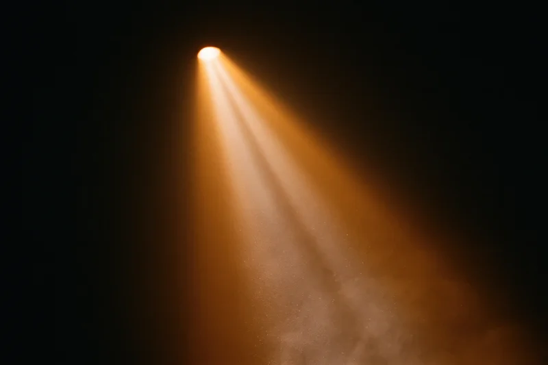 Warm amber spotlight beam shining downward through haze in dark theater space