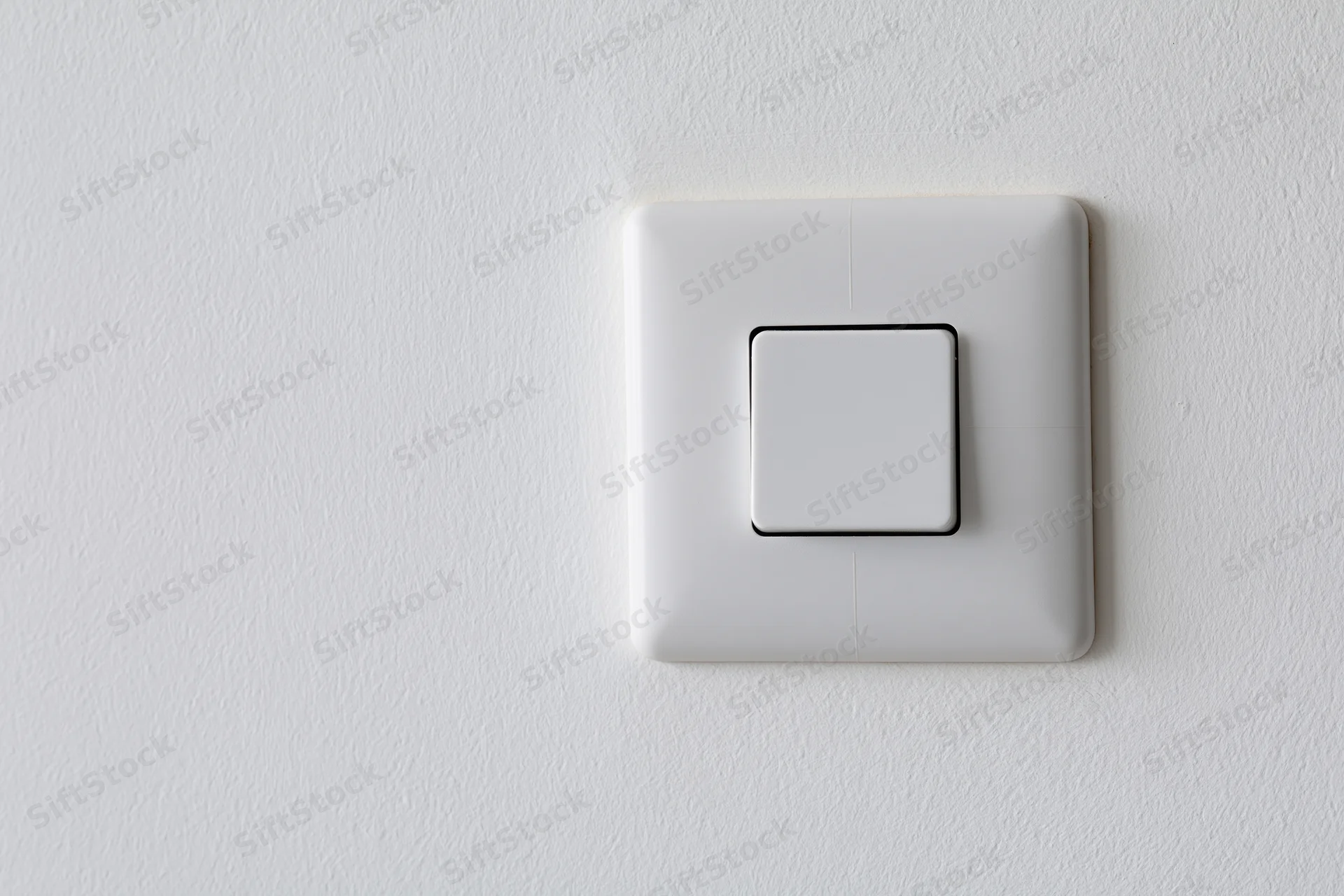 White square push-button light switch mounted flush on a textured white wall