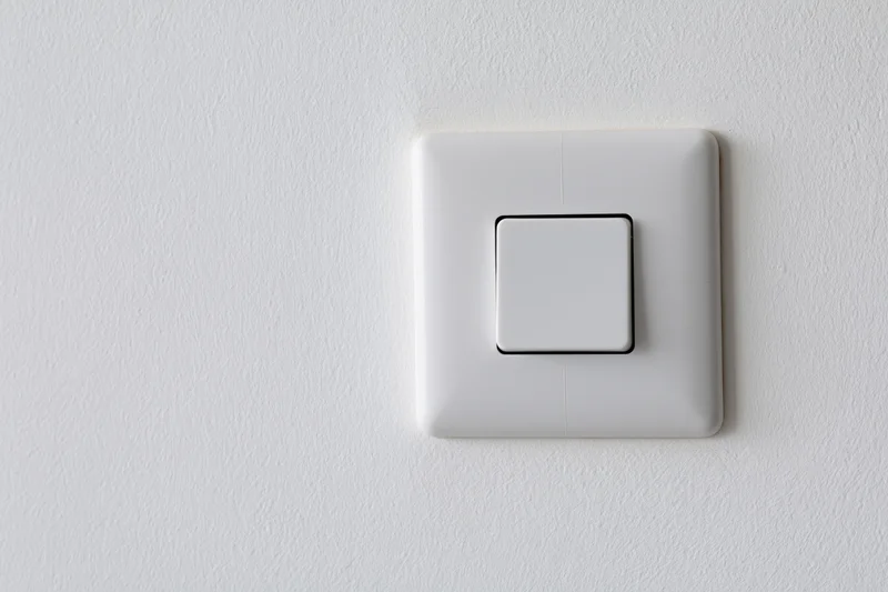 White square push-button light switch mounted flush on a textured white wall