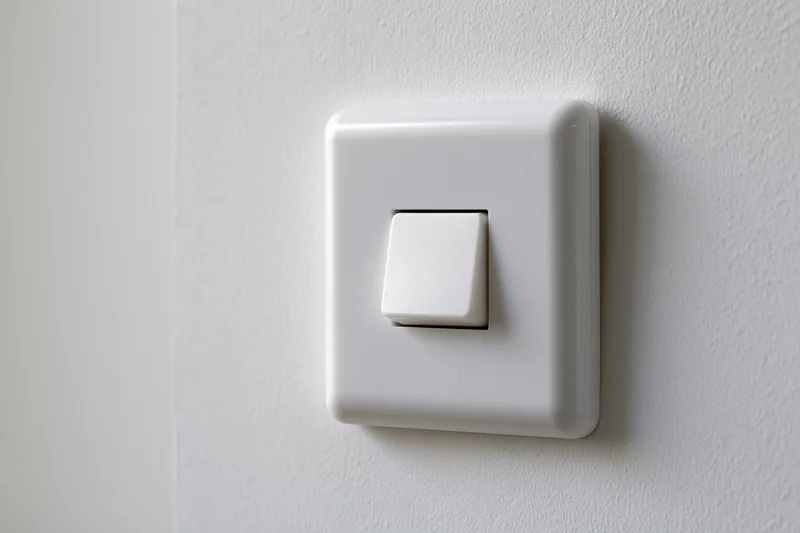 White square push-button light switch mounted on a textured wall in a home interior