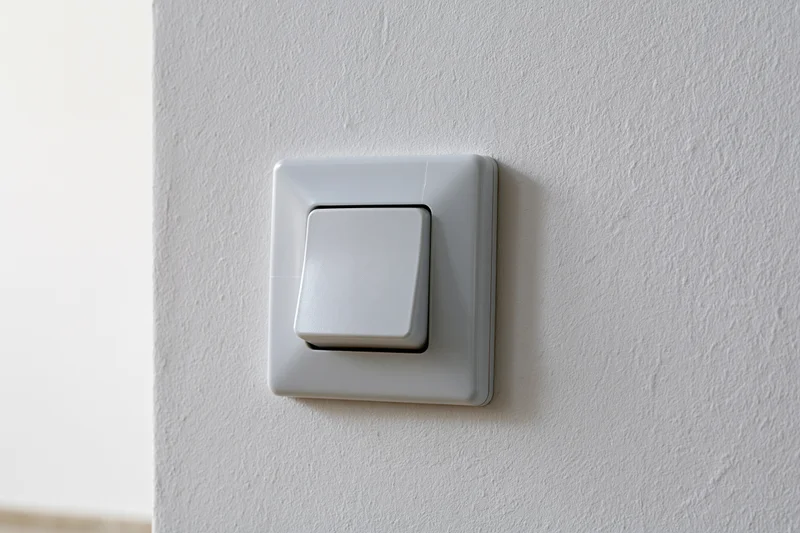 White square push-button light switch mounted on a textured wall in an interior space