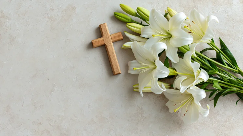 Wooden cross and white lilies arranged on a light surface with copyspace