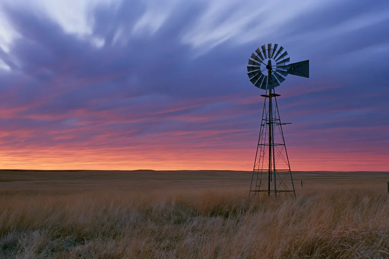 Steel farm windmill standing in open grassland at dusk