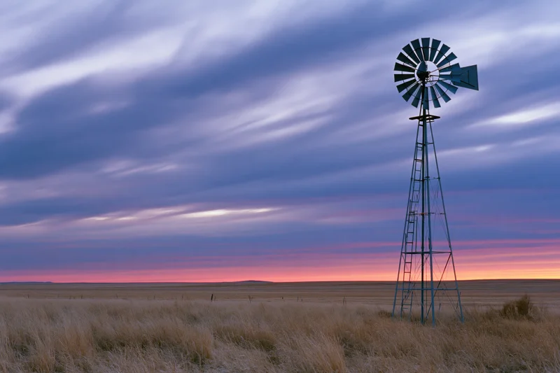 Steel farm windmill standing in flat open grassland at dusk