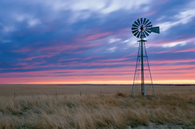 Steel farm windmill standing in flat open grassland at dusk