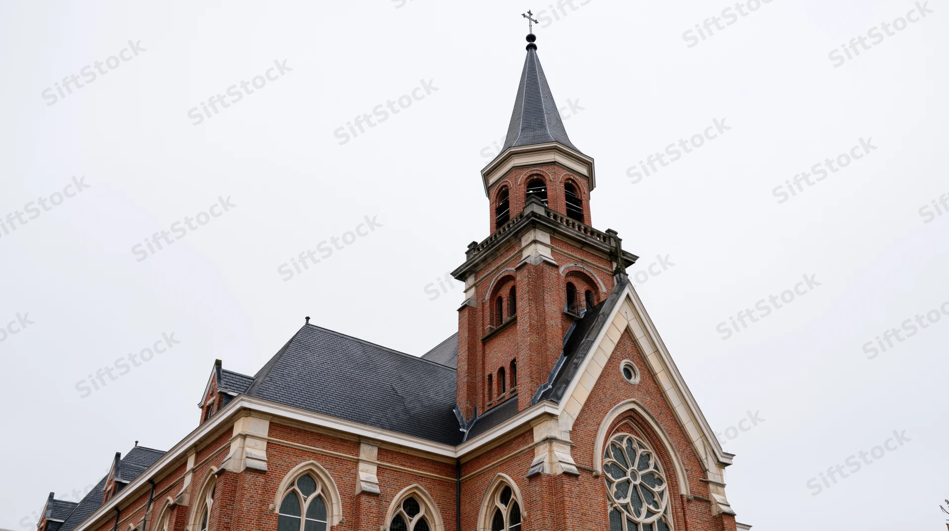 Red-brick christian church with tall steeple and arched windows under overcast sky