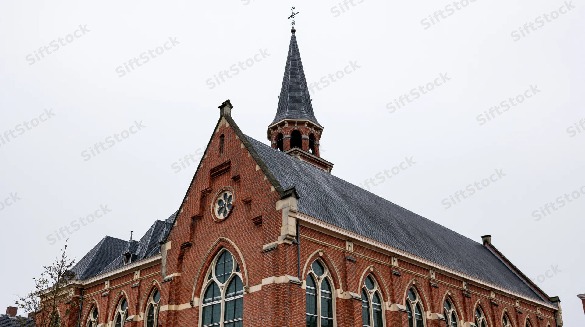 Red-brick christian church with tall steeple and arched windows under overcast sky