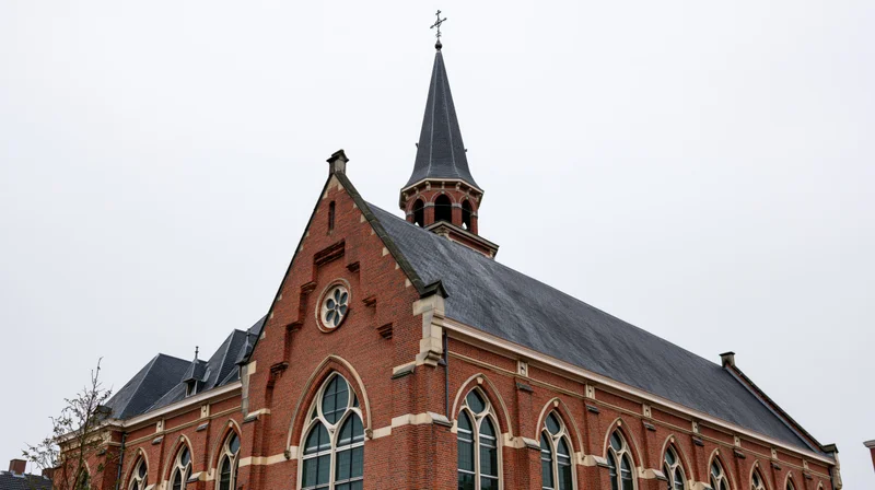 Red-brick christian church with tall steeple and arched windows under overcast sky