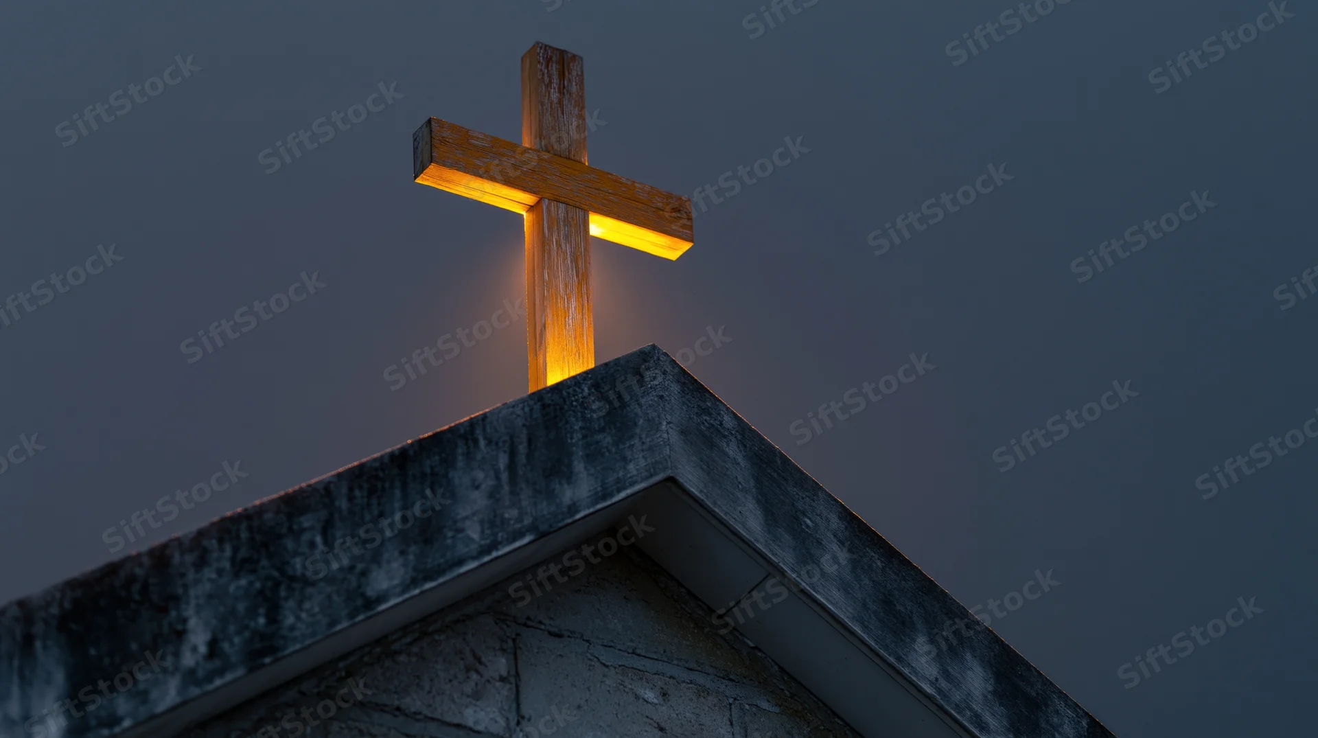 Illuminated wooden cross mounted on church roof peak at twilight