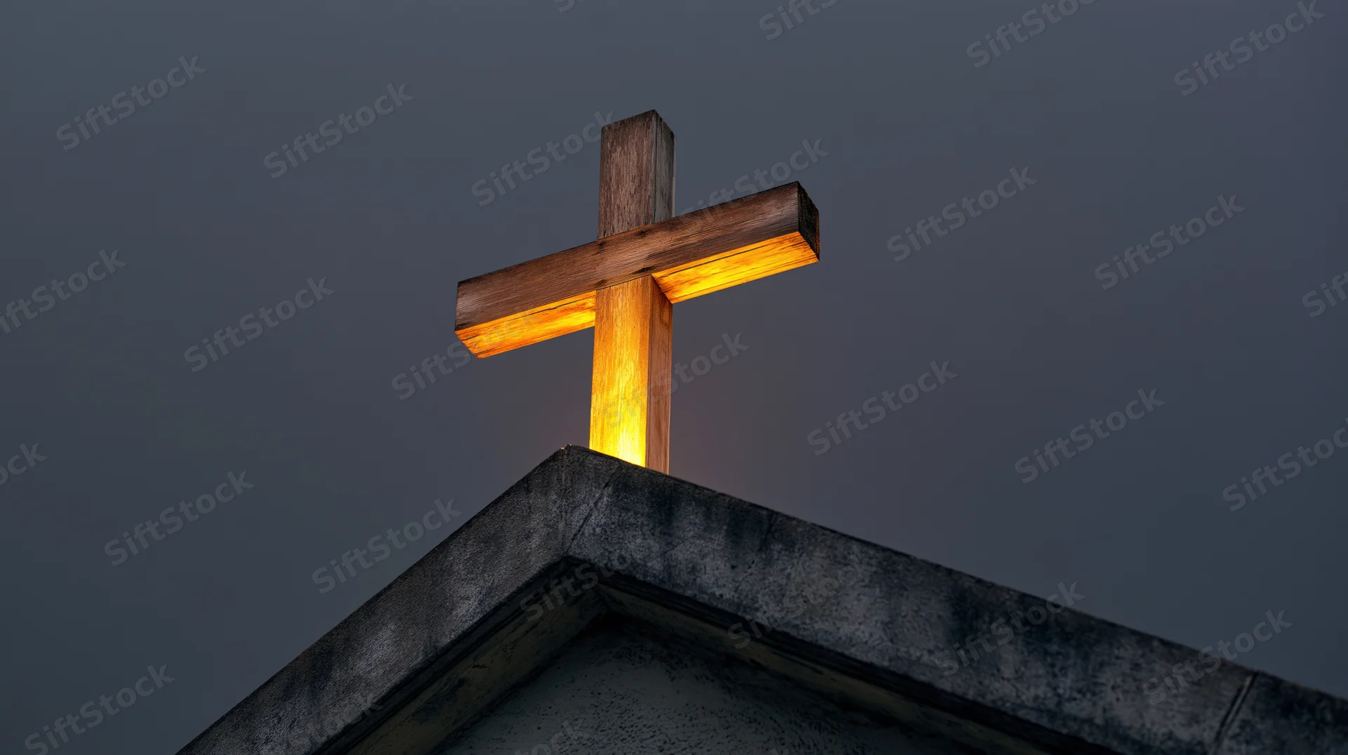 Illuminated wooden cross mounted on church roof peak at twilight