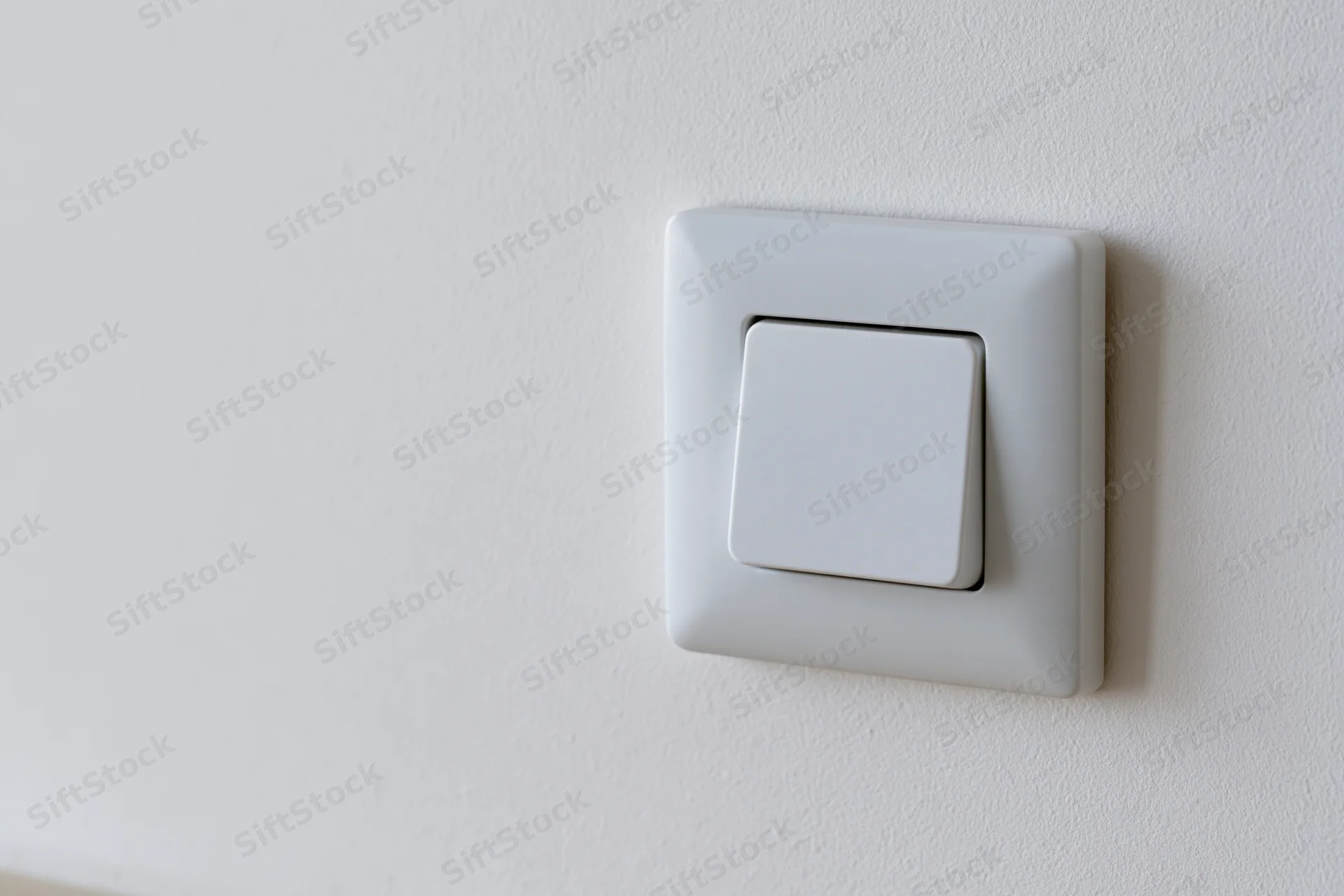 White square push-button light switch mounted on a plain white wall