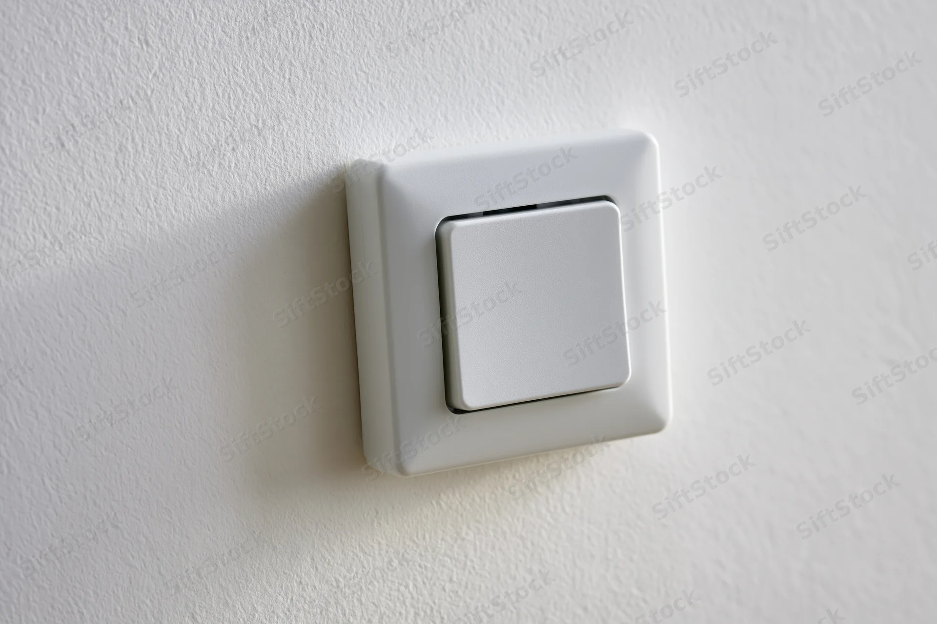 White square push-button light switch mounted on a flat white wall