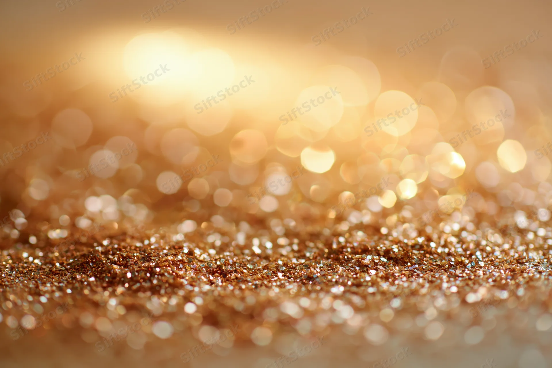 Scattered golden glitter particles on a textured surface with bokeh lights in the background