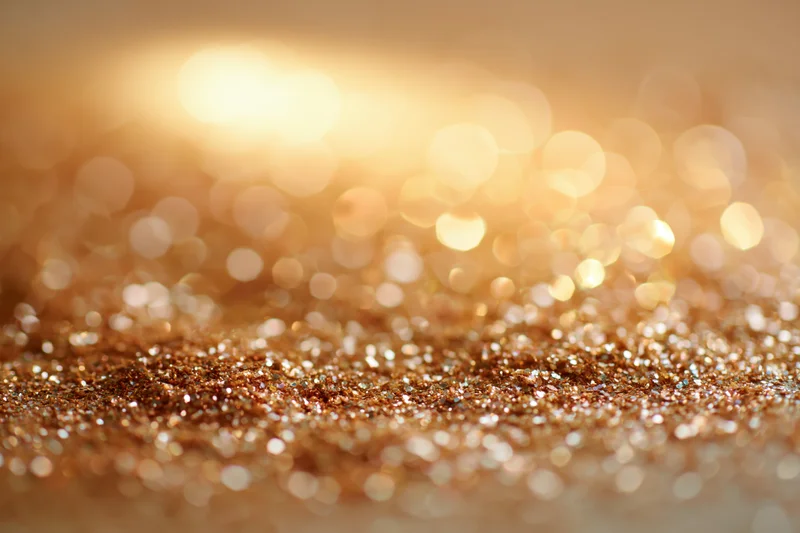 Scattered golden glitter particles on a textured surface with bokeh lights in the background