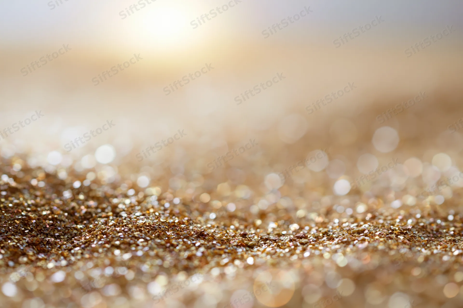 Scattered golden glitter particles on a textured surface with bokeh light reflections in the background