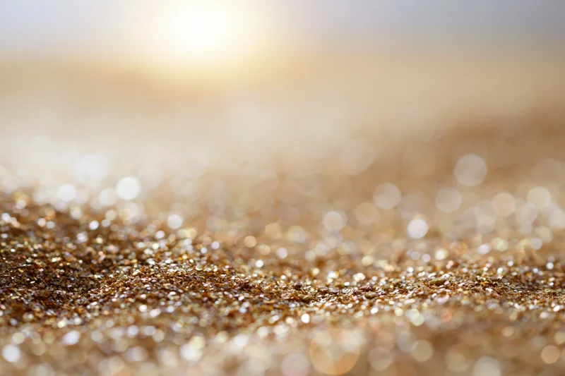Scattered golden glitter particles on a textured surface with bokeh light reflections in the background